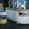 Tommee Tippee Super-Steam Advanced Electric Steriliser in white with a baby bottle and lid, showcasing its sleek design.