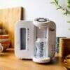 Tommee Tippee Perfect Prep Machine in white, placed on a wooden kitchen counter with colorful bowls and plants in the