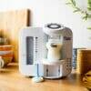 Tommee Tippee Perfect Prep Machine in white, dispensing warm formula into a bottle on a wooden countertop.