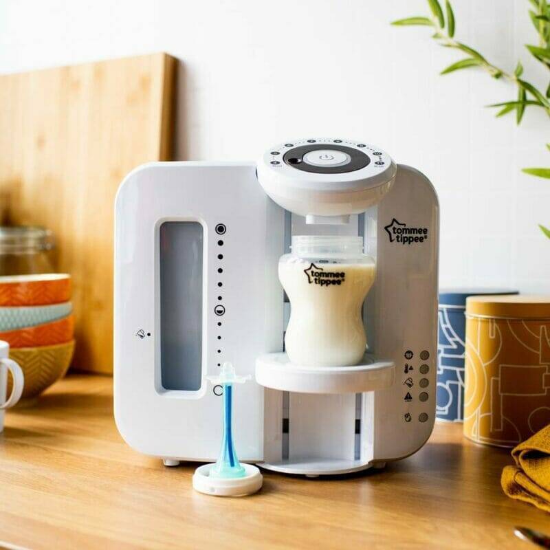 Tommee Tippee Perfect Prep Machine in white, dispensing warm formula into a bottle on a wooden countertop.