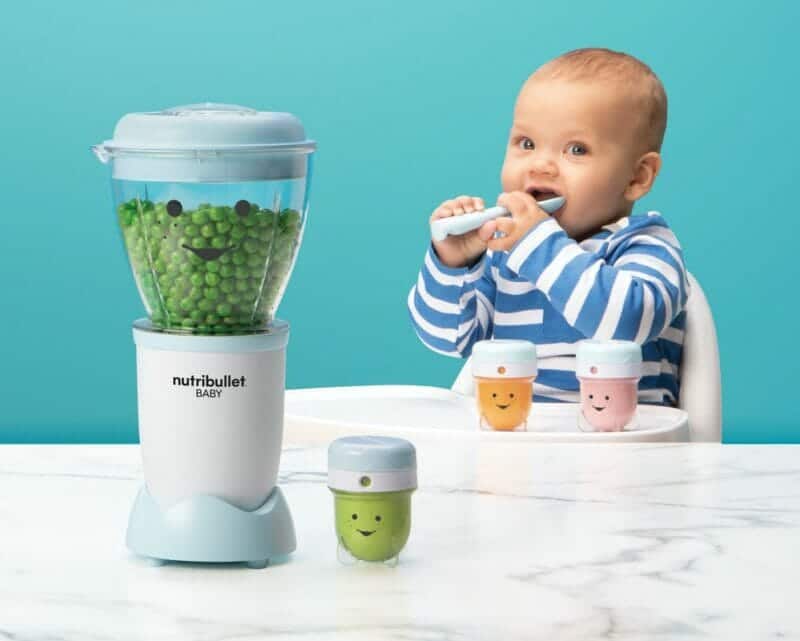 Nutribullet Baby blender in light blue with green peas, child sitting at table with colorful storage cups and spoon.