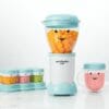 Nutribullet Baby blender in light blue with smiling face, surrounded by colorful storage cups on a marble countertop.