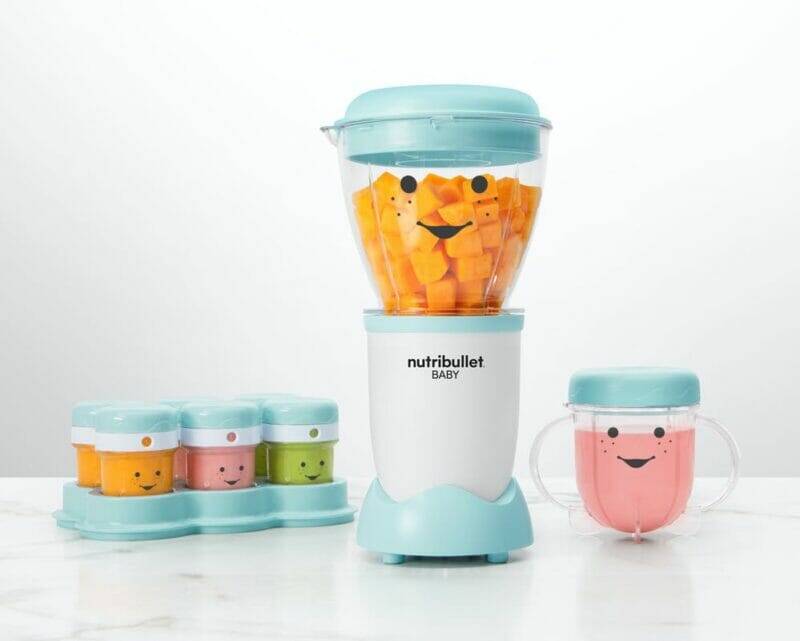 Nutribullet Baby blender in light blue with smiling face, surrounded by colorful storage cups on a marble countertop.