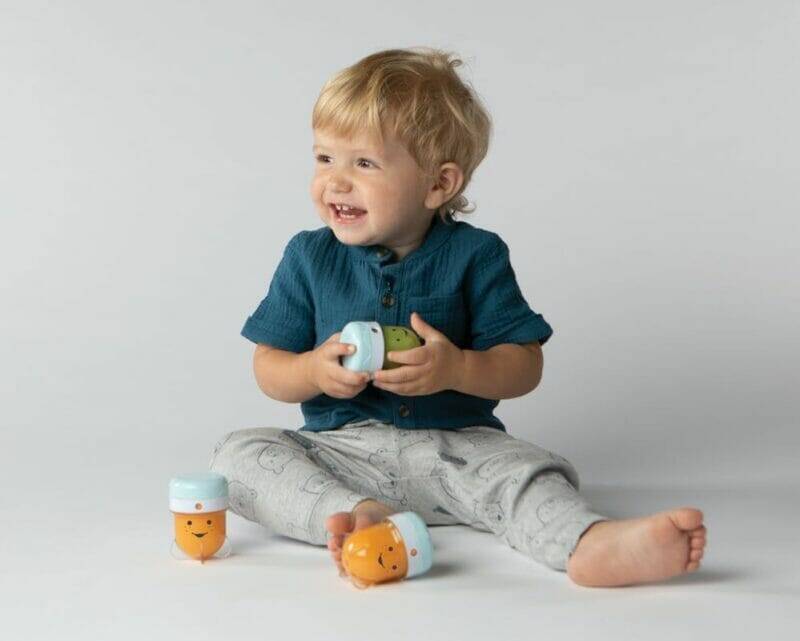 Nutribullet Baby in use with a smiling toddler holding colorful containers, sitting on a light background.