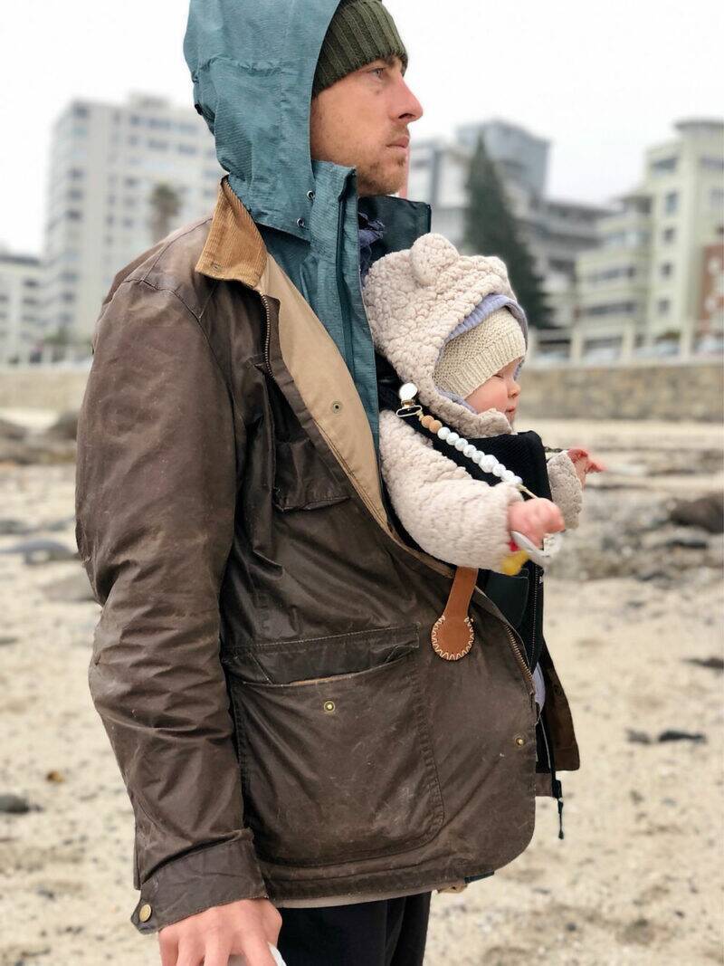 The Stella Clip in Beach Bébé, attached to a jacket, holding a baby snugly while outdoors on a beach.