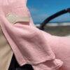 The Stella Clip in Beach Bébé attaches a soft pink blanket to a stroller, set against a beach backdrop.