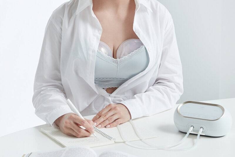 Spectra Handsfree Cup Set in use, featuring a woman wearing a nursing bra while writing at a desk.