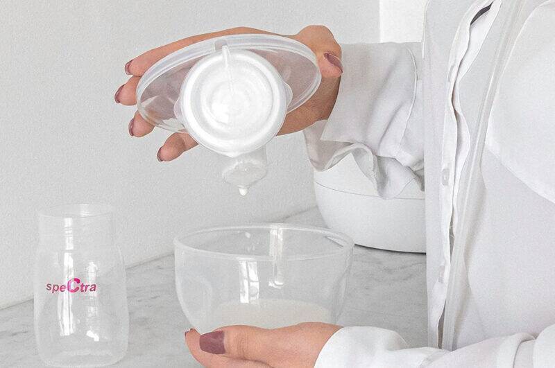Spectra Handsfree Cup Set in white, showing a user pouring milk into the collection cup, highlighting its practical design.