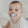 BIBS Infinity Pacifier in Blush and Vanilla, size 1, held by a smiling baby in a cozy setting.