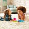 Munchkin Splash Cups in pink and blue, with two kids enjoying snacks on a cozy rug in a bright living room.