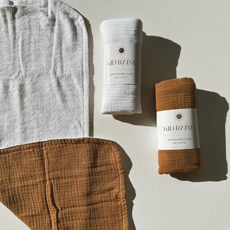 Kid Raine muslin towel-lined burp cloths in Harper white and Sienna brown, displayed on a light surface.