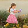 Munchkin Miracle 360° Sippy Cup in purple, held by a child in a polka dot shirt and pink skirt, walking in a garden.