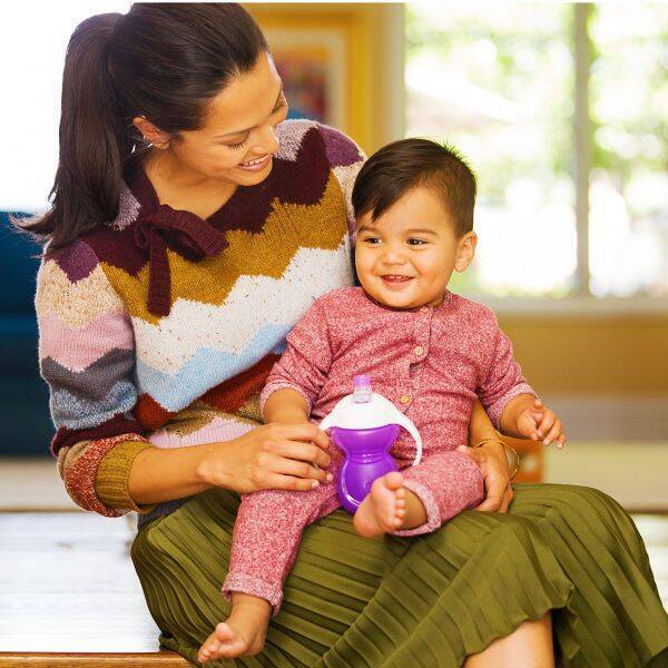 Munchkin Click Lock Bite Proof Trainer Cup in purple, held by a smiling child, seated with a woman in a cozy indoor setting.