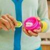Munchkin bottle and cup cleaning brush set in a bright pink container, being held by a person in a light sweater.