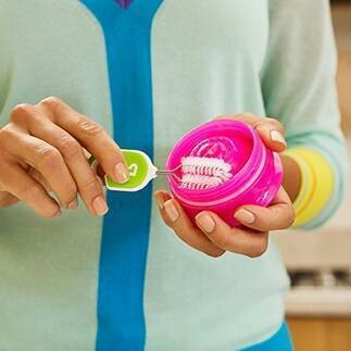 Munchkin bottle and cup cleaning brush set in a bright pink container, being held by a person in a light sweater.