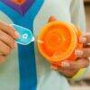Munchkin bottle and cup cleaning brush set in use, featuring a bright orange cup and blue brush detail for effective