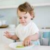 Baby Sense 2-in-1 Burp Cloth & Bib in white with small grey dots, worn by a toddler at a dining table.