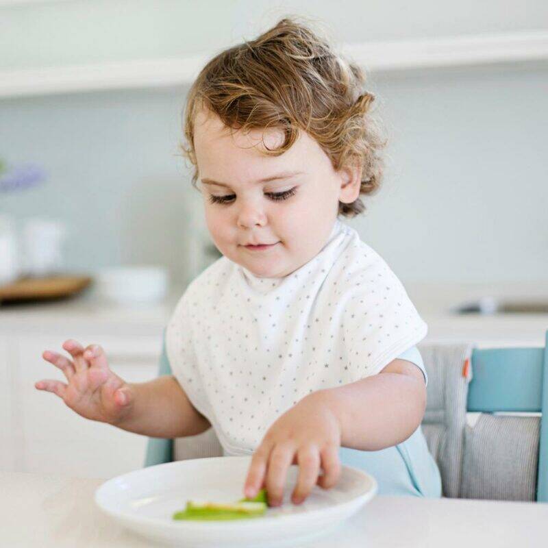 Baby Sense 2-in-1 Burp Cloth & Bib in white with small grey dots, worn by a toddler at a dining table.