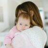 Baby Sense 2-in-1 Burp Cloth & Bib in pink, draped over a mother’s shoulder while she holds her baby.