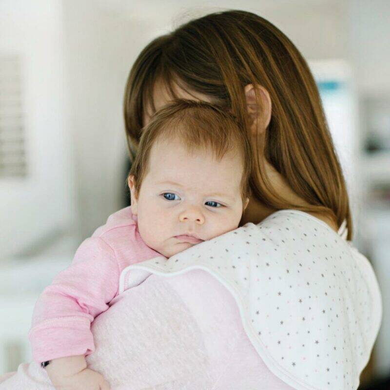 Baby Sense 2-in-1 Burp Cloth & Bib in pink, draped over a mother’s shoulder while she holds her baby.