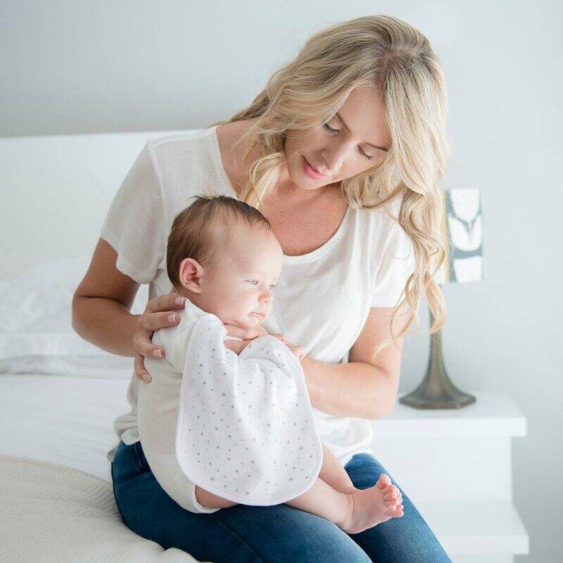 Baby Sense Burp Cloth Set in white with grey stars, shown being used by a mother holding her baby on a bed.