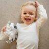 Baby Sense Taglet in blue and grey held by a smiling toddler lying on a soft surface, showcasing its playful design.