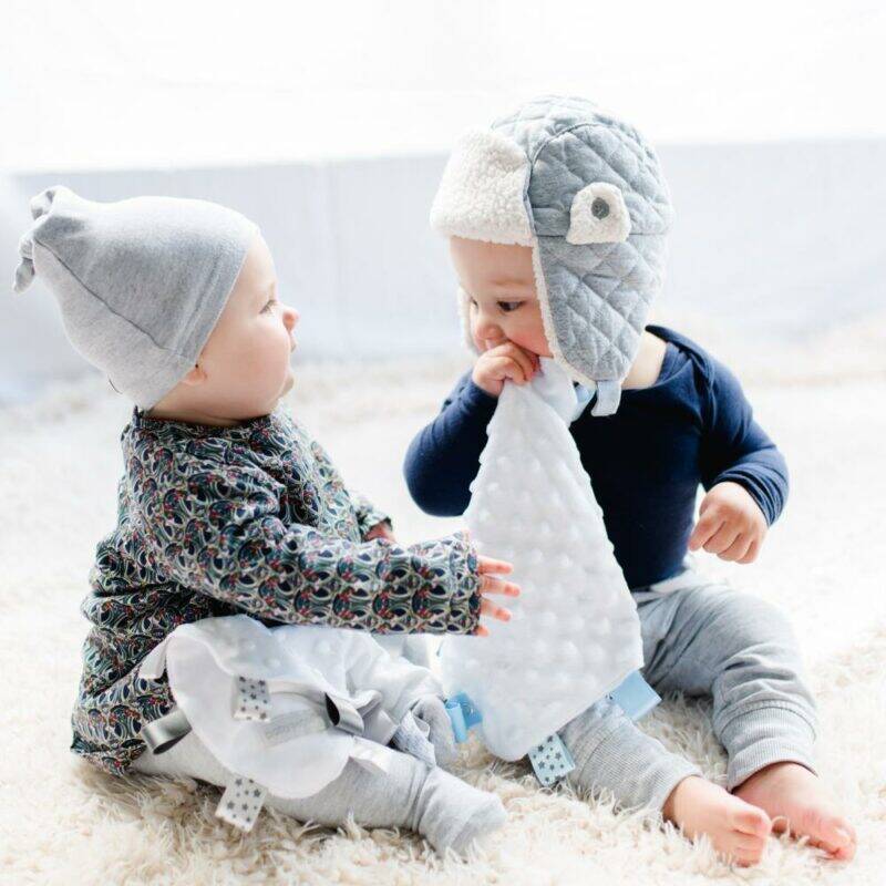 Baby Sense Taglet in blue and grey, featuring soft textures, with two babies interacting on a cozy rug.
