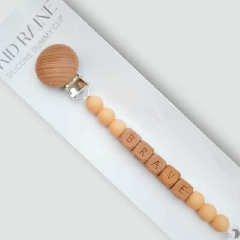 Kid Raine Affirmations Dummy Clip in neutral tones with wooden beads spelling "BRAVE" and a natural wood clip.
