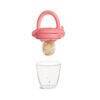 Munchkin Silicone Baby Food Feeder in pink, featuring a mesh pouch with food, hovering above a clear cup.