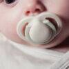 Tommee Tippee Newborn Soother 0-2m in grey and sage, gently cradled in a baby's mouth, showcasing its soft design.