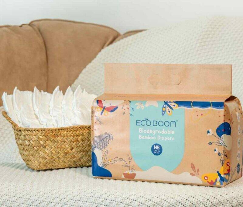 Eco Boom Joy Bamboo Baby Nappies for newborns, packaged in a colorful box, placed next to a basket of diapers.