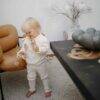Mushie Nature Teething Ring held by a child in a cozy living room, wearing a cream sweater and surrounded by soft decor.
