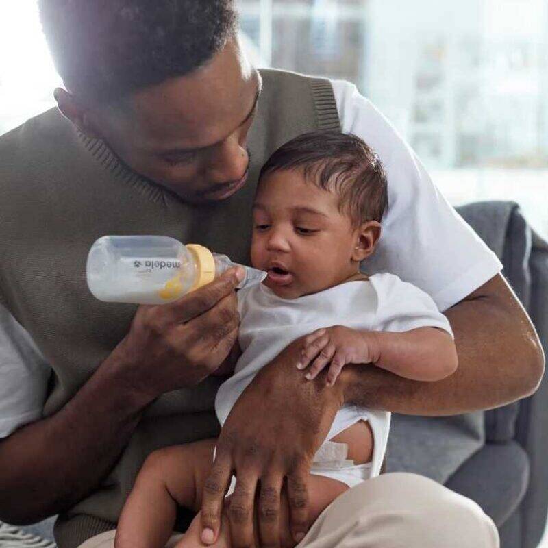 Medela Soft Cup Feeder in use, as a father feeds his baby in a cozy indoor setting.