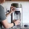 Baby Brezza Formula Pro Advanced in black, dispensing formula into a glass jar, showcasing its user-friendly design.