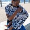 Maccie Stretch Cover in black and white zebra print, worn by a woman outdoors, providing comfort for a baby.