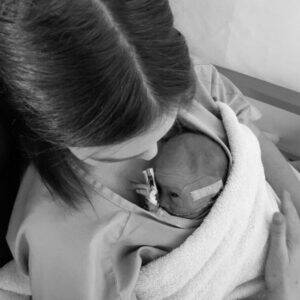 Mother holding a newborn baby wrapped in a towel, both looking peaceful in a caring embrace.
