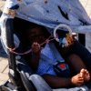 Maccie Anti-Drop Chain in pink, attached to a baby stroller, holding a toy while a child relaxes underneath a canopy.