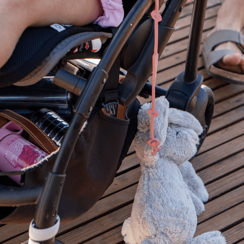 Maccie Anti-Drop Chain in pink, attached to a stroller, holding a stuffed bunny, showcasing practical use.