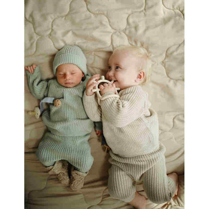Mushie No-Drop Sensory Teether in Blush, held by a baby in a cozy setting with another baby nearby.