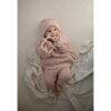 Mushie No-Drop Sensory Teether in blush, held by a smiling baby in cozy knitwear, lying on a soft blanket.