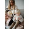 Mushie Silicone Training Cup in Blush held by a child sitting next to a parent, who is holding a baby. Cozy indoor setting.