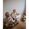 Mushie Silicone Training Cup and Straw in Bees color, used by a toddler at a dining table with snacks.