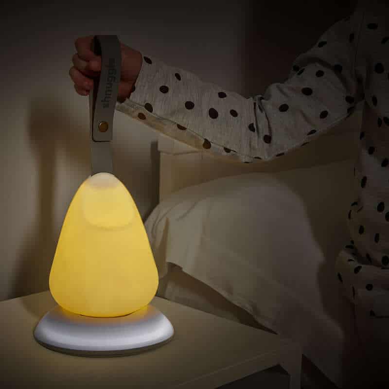 Shnuggle Moonlight Night Light in soft yellow, held by a child, glowing gently on a bedside table.