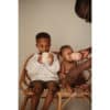Mushie Silicone Training Cups in Bees and Blush, with kids enjoying drinks on a rattan bench.