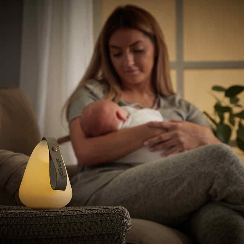 Shnuggle Moonlight Night Light in soft yellow, illuminating a cozy scene with a mother holding her baby on a sofa.