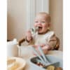 Mushie Silicone Fresh Food Feeder in Sage, used by a baby in a high chair, enjoying food from a bowl.