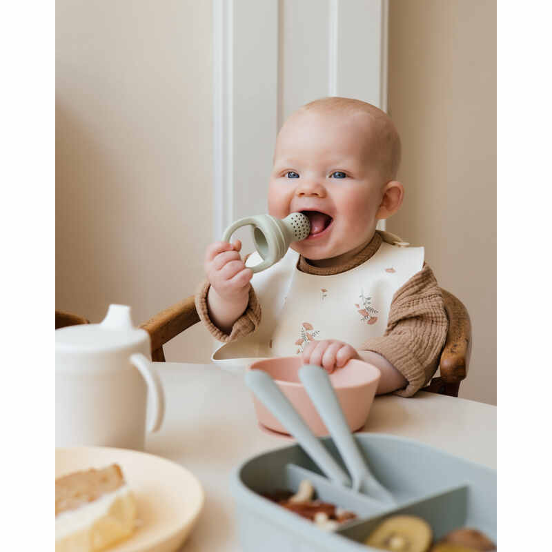Mushie Silicone Fresh Food Feeder in Sage, used by a baby in a high chair, enjoying food from a bowl.