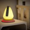 Shnuggle Moonlight Night Light in soft yellow, shaped like a teardrop, placed on a bedside table next to a crib.