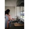 Mushie Silicone Baby Bottle Brush in blush, held by a mother in a kitchen while caring for her baby.