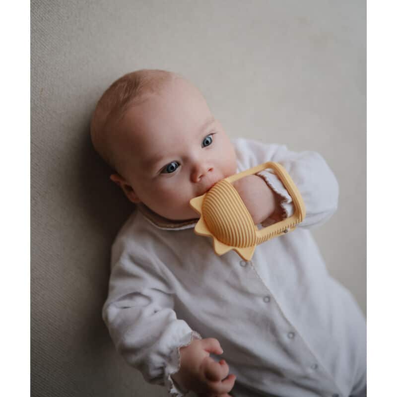 Mushie No-Drop Sun Teether in Sunshine color, held by a baby, featuring a sun shape and textured grip.